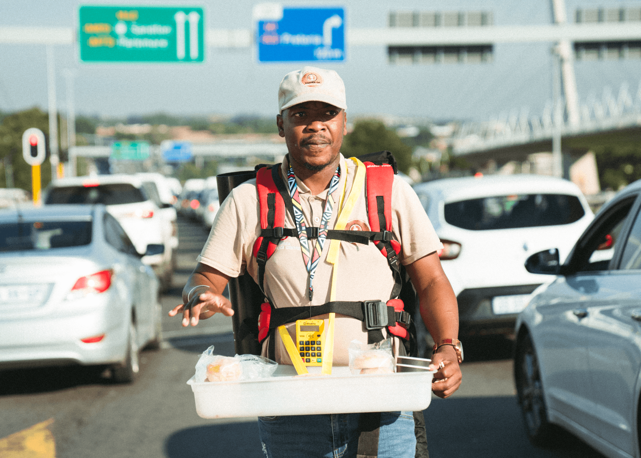 Street vendor walking between cars selling food and drinks, carrying a mobile card machine.