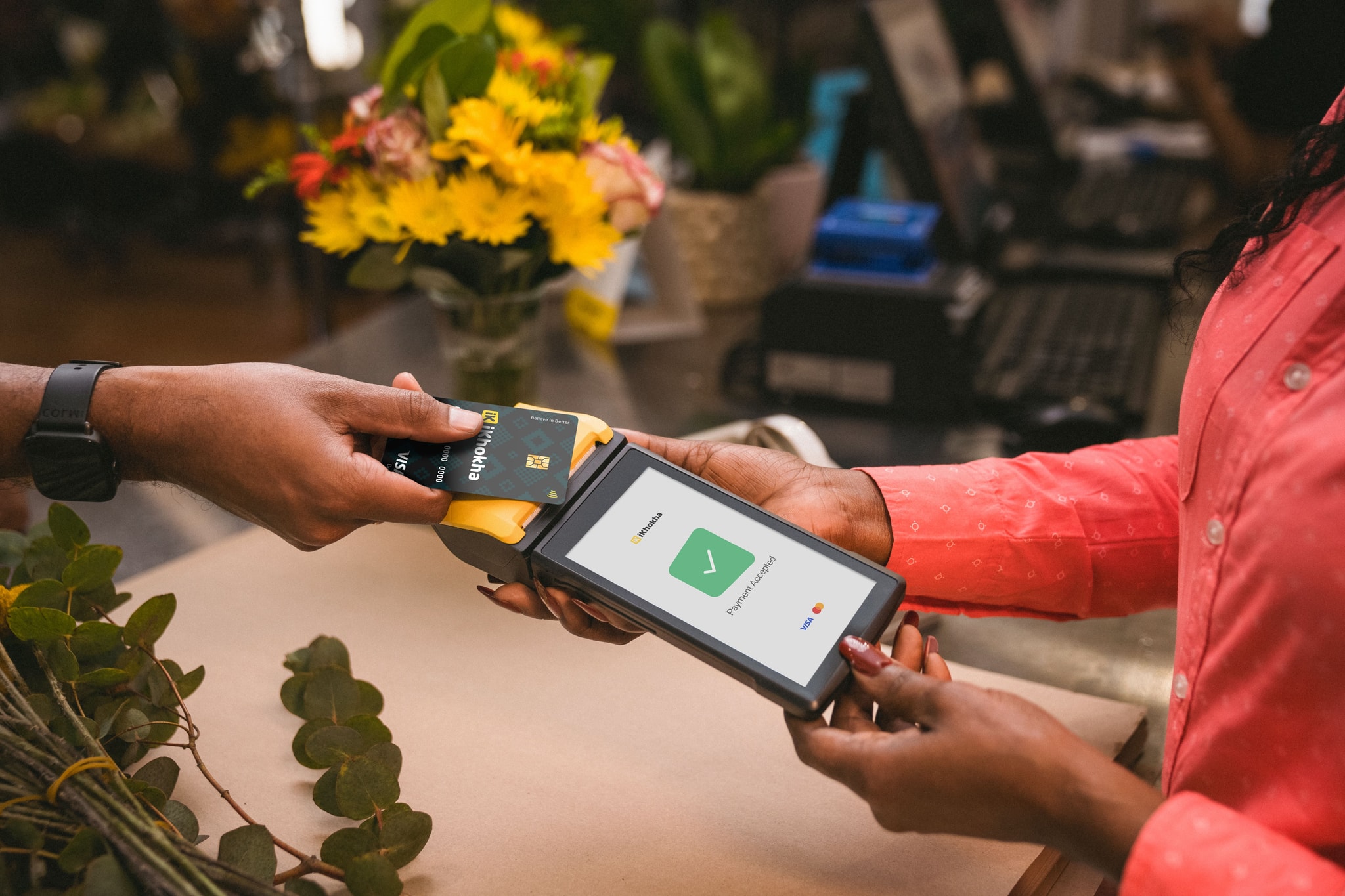 Customer making a contactless card payment on a iKhokha portable card machine at a flower shop counter.